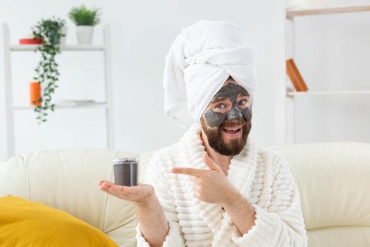 Bearded man having fun with a cosmetic mask on his face made from black clay. Men skin care and spa at home.