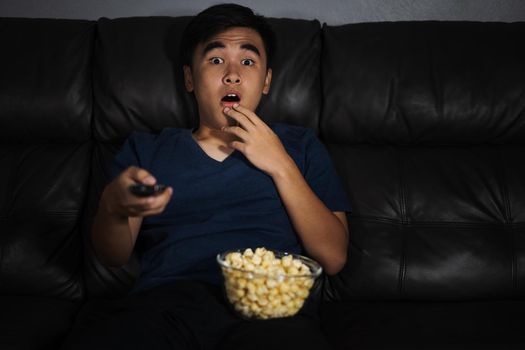 Shocked young man watching at tv and sitting on sofa in the living room at night