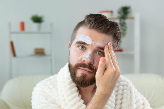 Bearded guy applying anti-wrinkle cream on his face. Skin care and spa for man concept