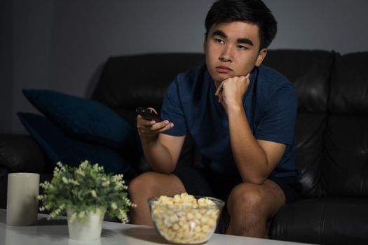 young bored man watching tv and sitting on sofa in the living room at night