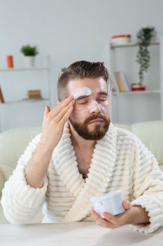 Closeup of handsome young man applying facial cream in front of mirror