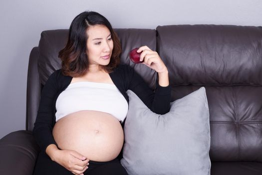 portrait of pregnant woman resting with red apple at home on sofa