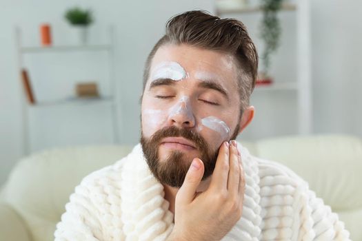 Bearded guy applying anti-wrinkle cream on his face. Skin care and spa for man concept