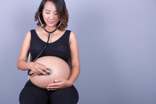 pretty young pregnant asian woman with stethoscope listening belly to baby