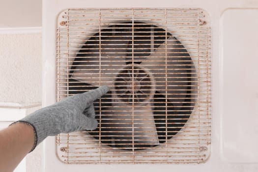 The hand of an air conditioner repair and maintenance specialist in a construction glove working with air-conditioned old equipment.