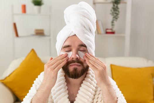 Bearded man applying eye patches on his face. Wrinkles and face home care for men
