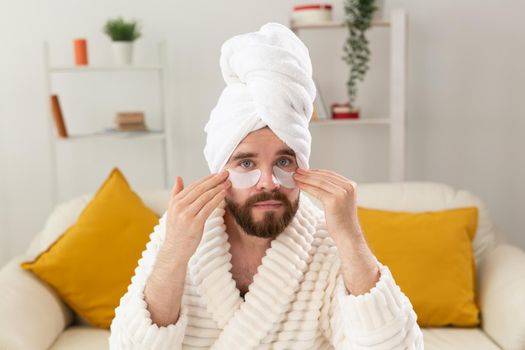 Bearded man applying eye patches on his face. Wrinkles and face home care for men
