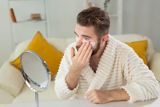 Bearded man applying eye patches on his face. Wrinkles and face home care for men