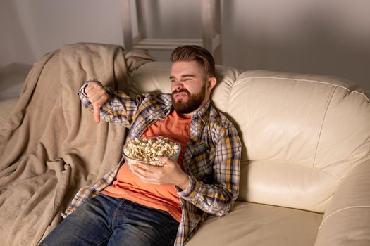 Bearded man watching film or sport games TV eating popcorn in house at night. Cinema, championship and fan.