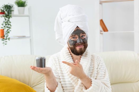 Bearded man having fun with a cosmetic mask on his face made from black clay. Men skin care and spa at home.