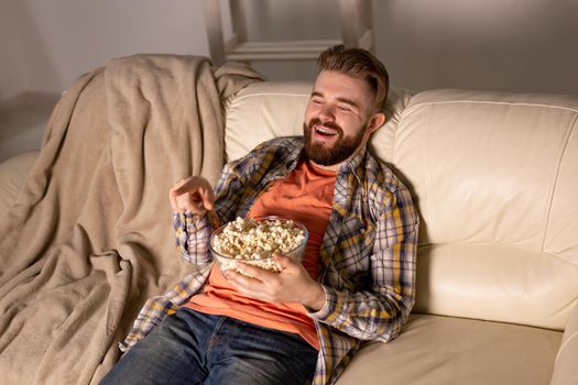 Bearded man watching film or sport games TV eating popcorn in house at night. Cinema, championship and fan.