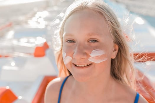 Close-up portrait of the face of a young positive attractive girl with sunscreen and sun protection on her cheeks.