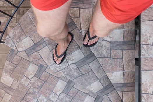 Men's legs in black flip flops and red shorts go down and walk down the stairs. Walking style.