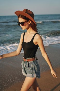 cheerful woman in sunglasses and a hat walks along the ocean. High quality photo