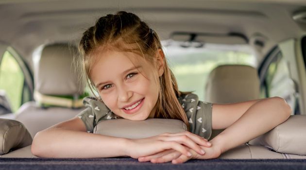 Cute preteen girl with hairstyle sitting in the car, looking at the camera and smiling. Child kid in the vehicle inside during summer trip