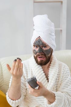 Bearded man has clean fresh skin, wears beauty clay mask on face and enjoys beauty treatments. Spa at home, body and skin care.