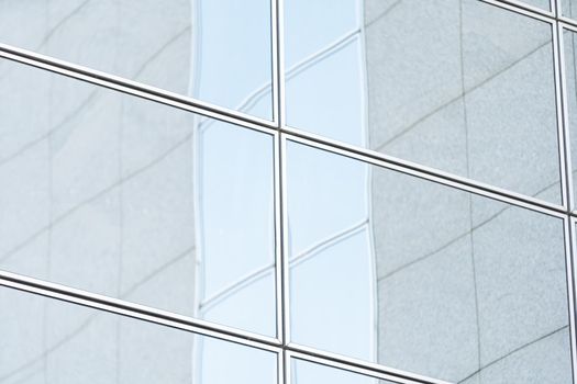 Perspective and underside angle view to textured background of modern glass building skyscrapers over blue cloudy sky.