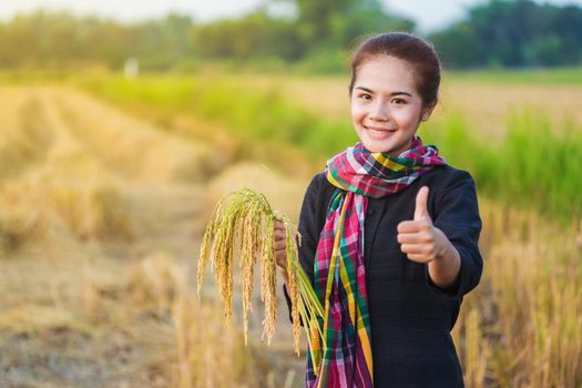 woman showing thumb up and holding rice in field, Thailand