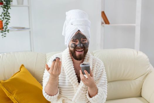 Bearded man having fun with a cosmetic mask on his face made from black clay. Men skin care and spa at home.