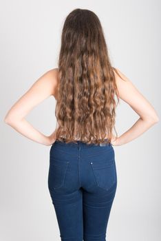 Back view of young woman with long hair wearing white t-shirt and blue jeans on white background