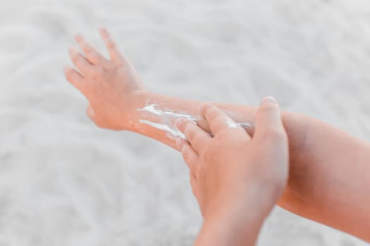 The hand of a young girl smears sunscreen and sun protection on the second hand against the background of the beach, close-up.