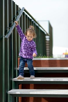 Little 20-month-old girl going down some stairs outdoors