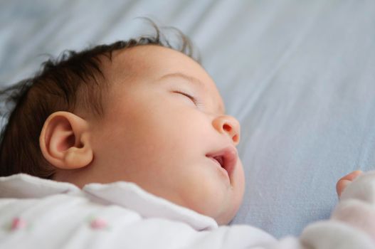 Newborn baby girl sleeping on blue sheets at home