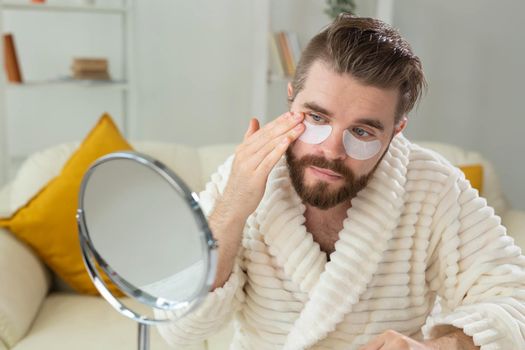 Bearded man applying eye patches on his face. Wrinkles and face home care for men
