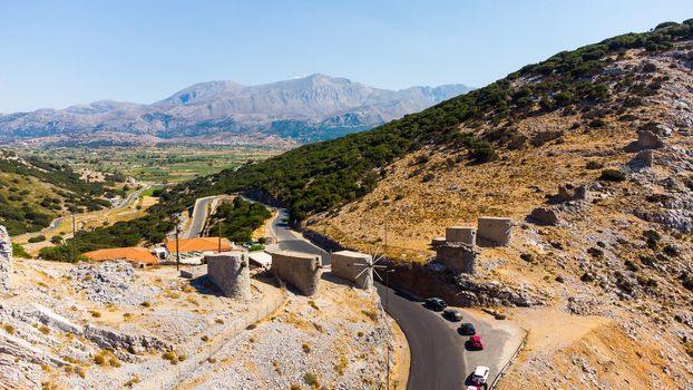 a panoramic view of the ancient centuries-old mills against the backdrop of mountains and olive groves of Crete filmed from a drone