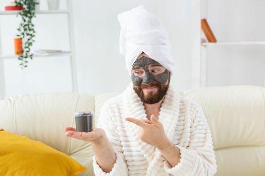 Bearded man having fun with a cosmetic mask on his face made from black clay. Men skin care and spa at home.