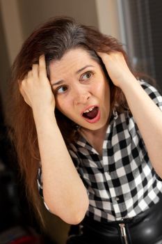 Horrified young woman looking in the bathroom mirror staring open mouthed at the first grey hair on her scalp, a first sign of ageing, or noticing that she is suffering from dandruff