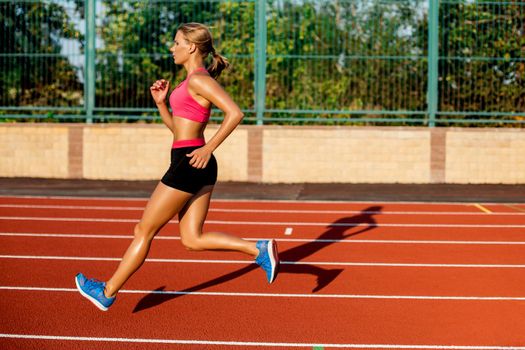 Side view beautiful young woman exercise jogging and running on athletic track on stadium. Sport, healthy lifestyle concept.