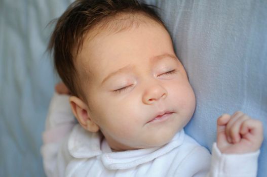 Newborn baby girl sleeping on blue sheets at home