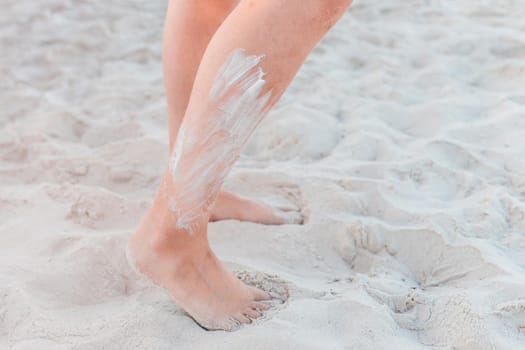 The legs of a young girl stand on the beach white sand with sunscreen on the skin.