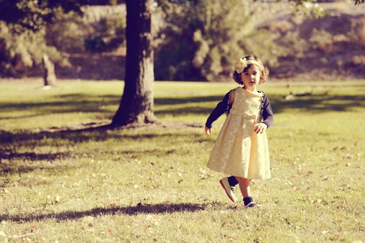 Portrait of a little girl running and playing in the park wearing a beautiful dress