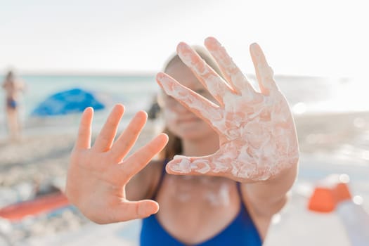 A young European teenage girl stretched her arms forward with sunscreen and sun protection on her palms against the backdrop of a sea beach.