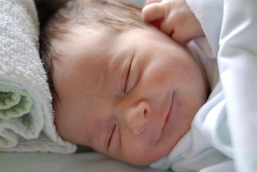 Newborn baby girl in hostpital bed sleeping and smiling. Caucasian female.