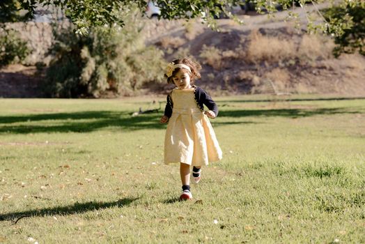 Portrait of a little girl running and playing in the park wearing a beautiful dress