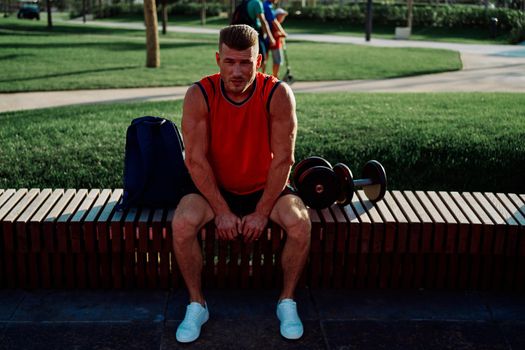 Cheerful male athlete in the park sits on a bench. High quality photo