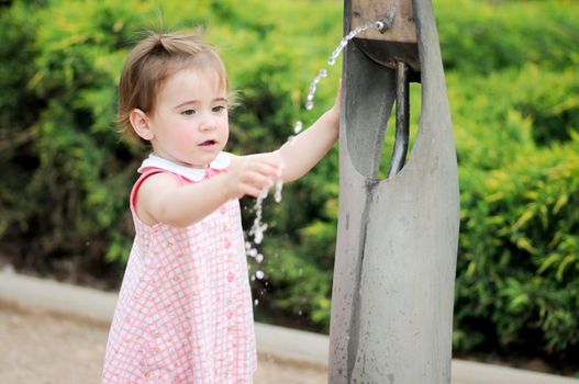 Adorable little girl drinking water in a park fountain