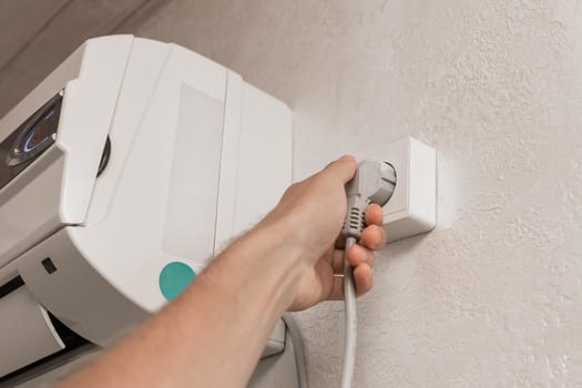 The hand disconnects or plugs the air conditioner power plug on the wall in the room from the outlet.