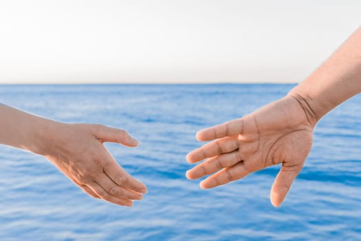 The man's hand reaches for the woman's hand against the background of the sea. Romantic Relationships and Friendship Concept.