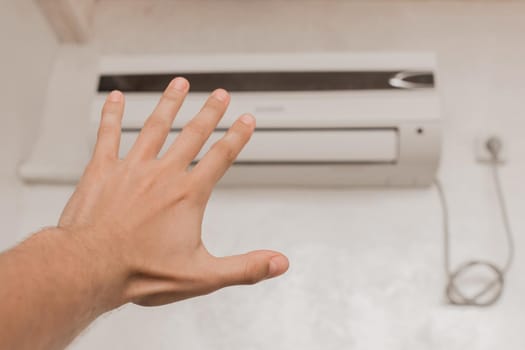 The guy puts his hand under the air conditioner in the room to check the temperature and the feeling of warm or cold air.