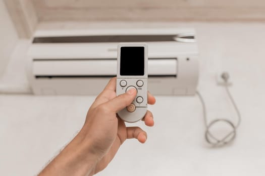 The guy's hand holds the remote control of the air conditioner. Cooling and temperature control in the room of the house.