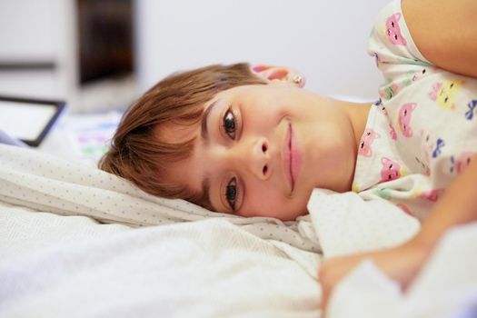 Happy little girl, eight years old, lying on her bed at home. smiling to camera.