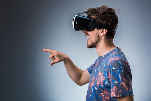 Side view of a young guy using a VR headset on a gray background. Studio shoot. Emotions
