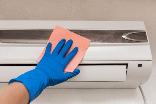 The hand of a man in a blue rubber household glove wipes and cleans the air conditioner. Maintenance and cleaning indoor service.