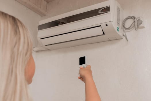 Young girl blonde teenager holds in his hands a remote control of air conditioning in the interior of the room.