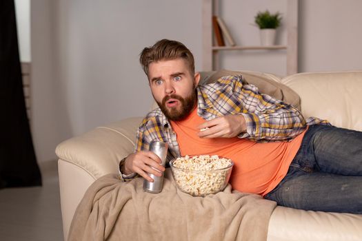 Bearded man watching film or sport games TV eating popcorn in house at night. Cinema, championship and fan.