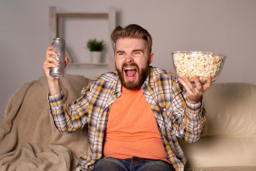 Bearded man watching film or sport games TV eating popcorn in house at night. Cinema, championship and fan.